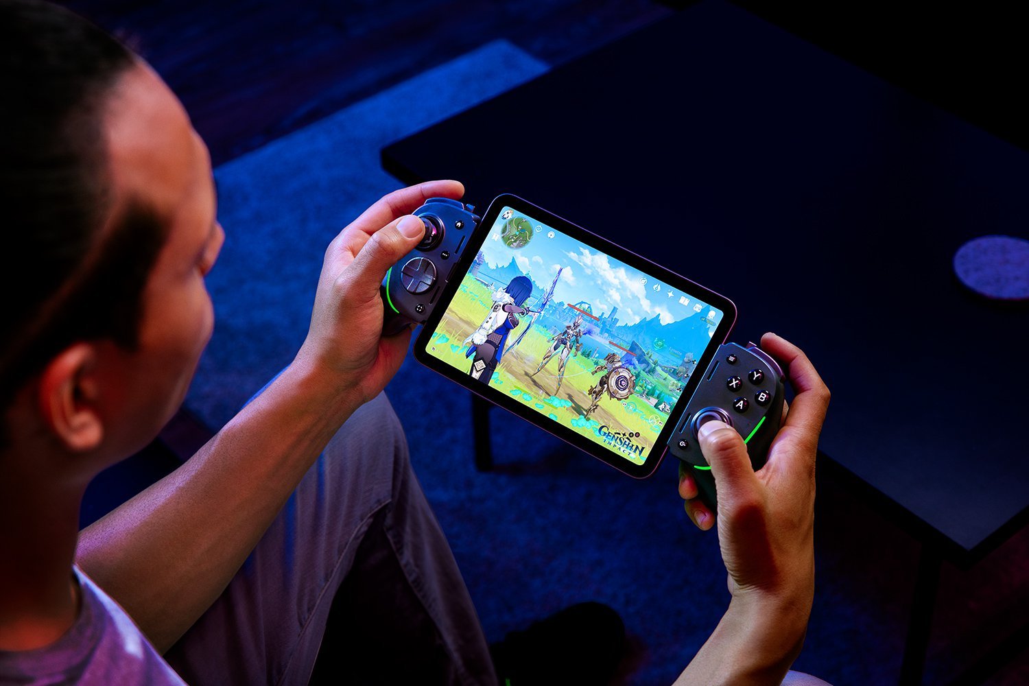 A man playing Genshin Impact on an iPad mini with a Razer Kishi Ultra gaming controller attached.