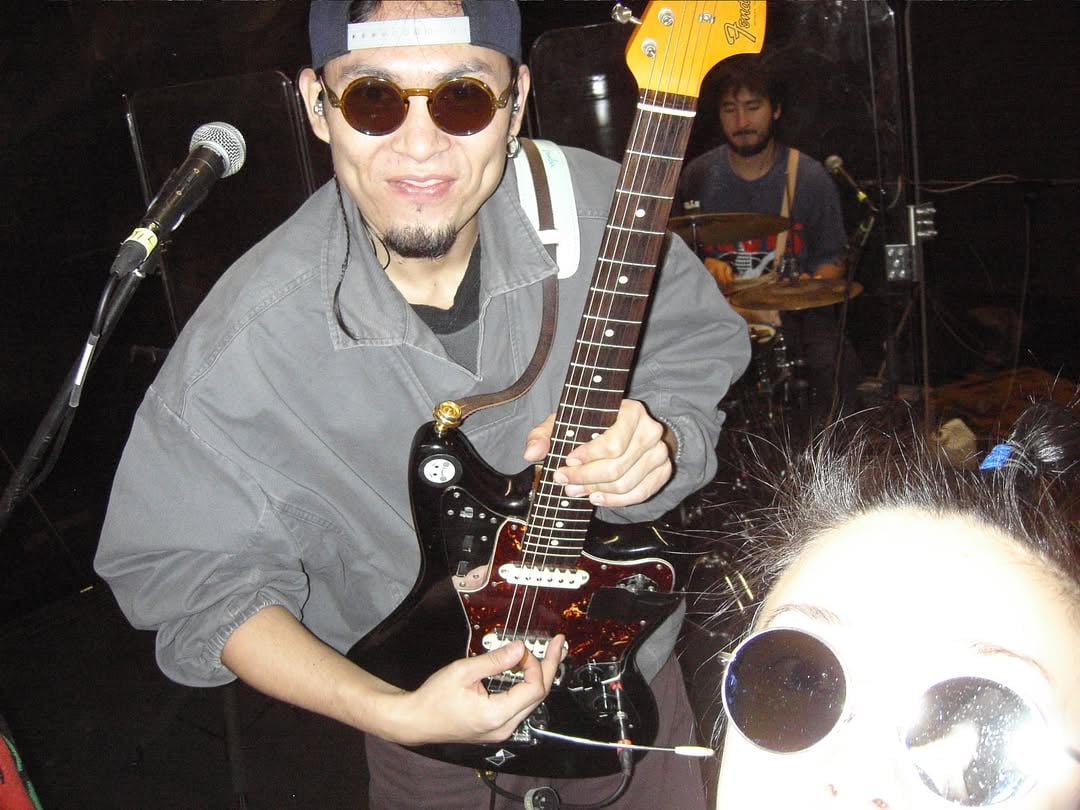 Members of Mola Oddity performing onstage with instruments under colored concert lighting.