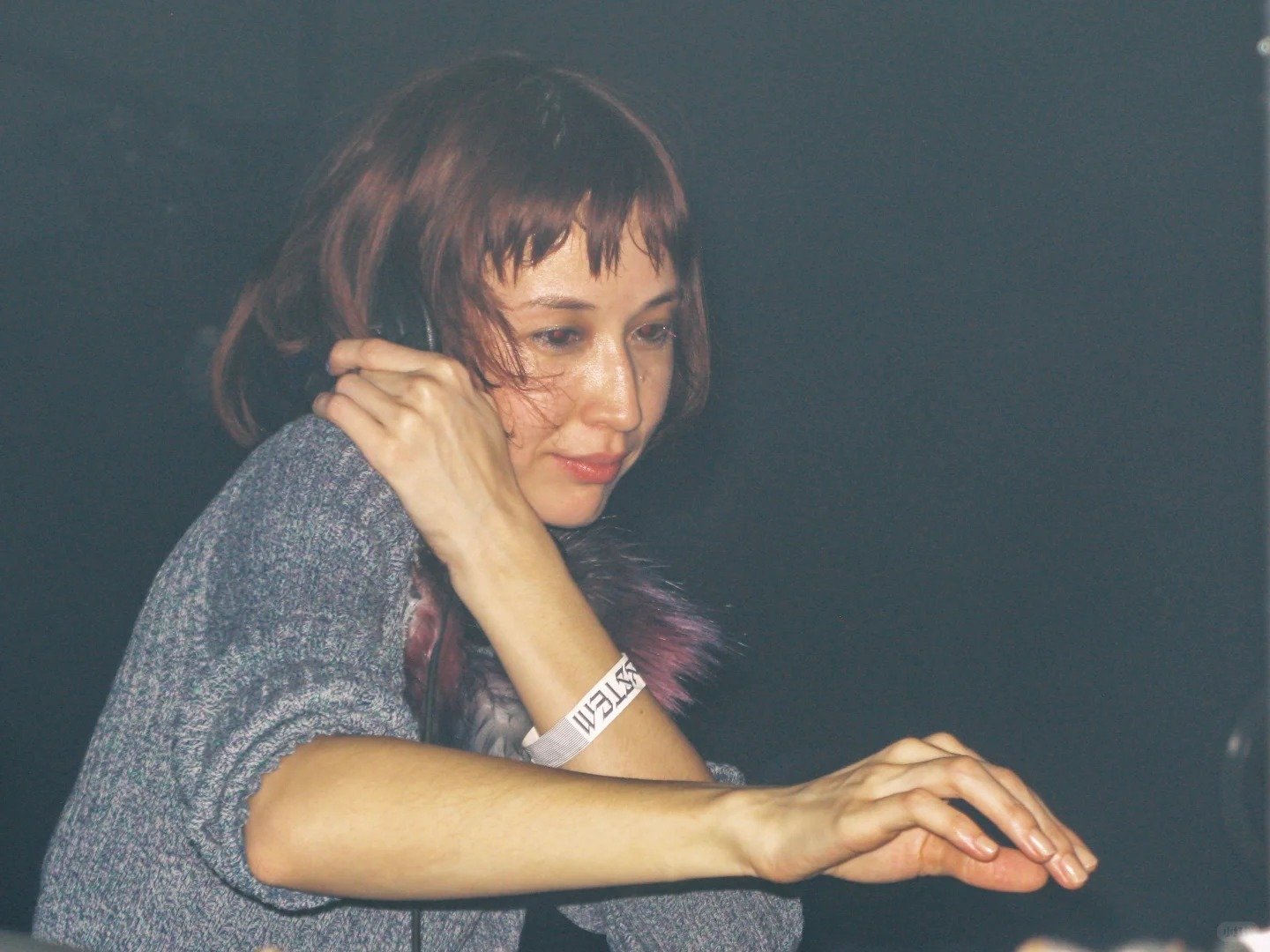 Ashley Yuka behind the DJ booth wearing a colorful outfit while playing music for a dancing crowd.
