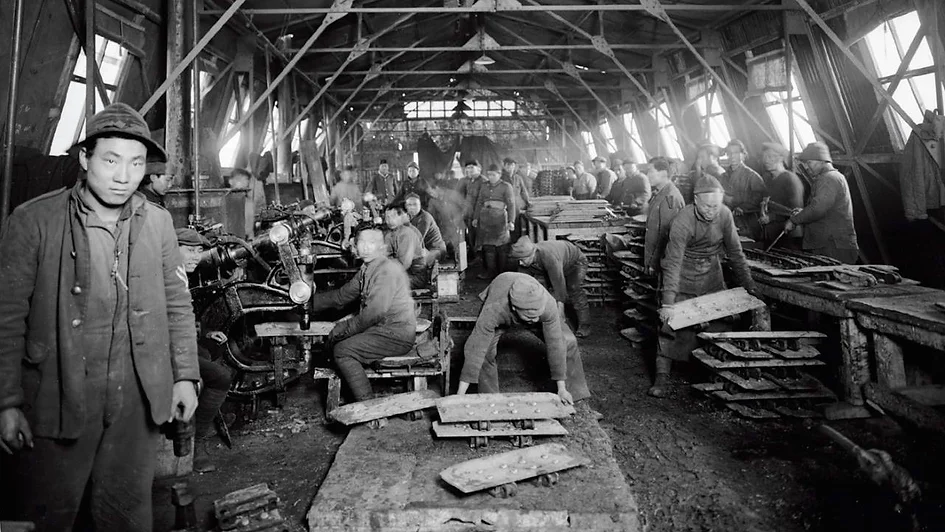 Chinese dock workers in Rotterdam in the 1910s standing near the harbor, dressed in early 20th century work clothes with ships and port infrastructure in the background.